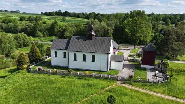 Aerial drone view of Chlina village in Silesian Voivodeship, Poland, featuring historic church, agricultural fields and rural countryside landscape during a sunny spring season. Church near the lake