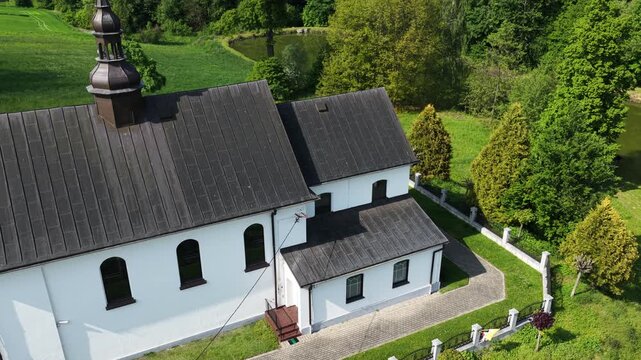 Aerial drone view of Chlina village in Silesian Voivodeship, Poland, featuring historic church, agricultural fields and rural countryside landscape during a sunny spring season. Church near the lake