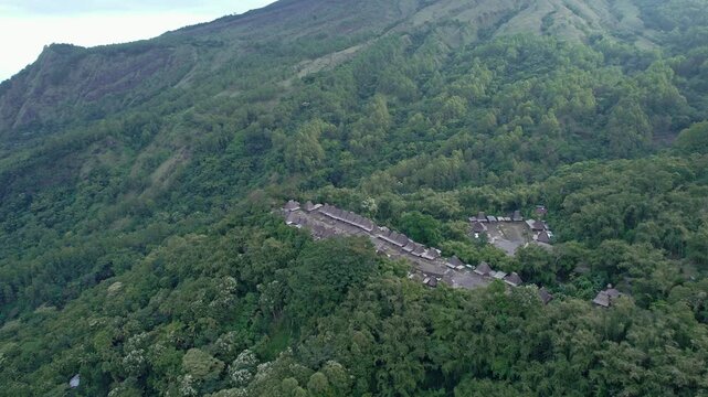 Aerial view of Bena Traditional Village with its iconic thatched roofs nestled among lush green forests and mountain slopes in Kecamatan Jerebuu, Nusa Tenggara Timur, Indonesia.
