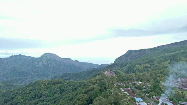 Aerial view of Bena Traditional Village with thatched roof houses nestled among lush green hills and misty mountains in Kecamatan Jerebuu, Nusa Tenggara Timur, Indonesia.