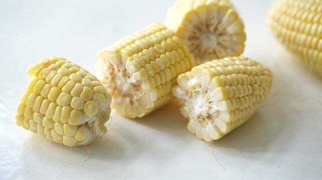 Fresh yellow sweet corn cut into sections with loose kernels scattered on a white surface, showcasing a natural and nutritious ingredient ready for cooking or consumption