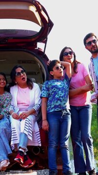 Indian family sitting in car dicky outdoors ready to go for picnic enjoying fun moments, grandparents, parents, and kids relaxing together, sharing laughter and bonding during a joyful outdoor break