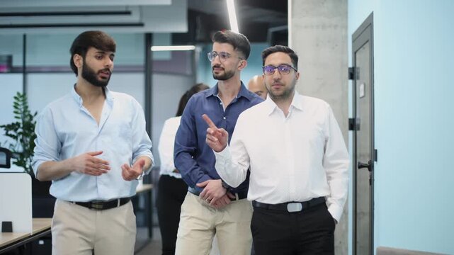 Three men are walking down a hallway, one of them is wearing a blue shirt