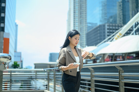 Businesswoman checks smartwatch while walking in modern city