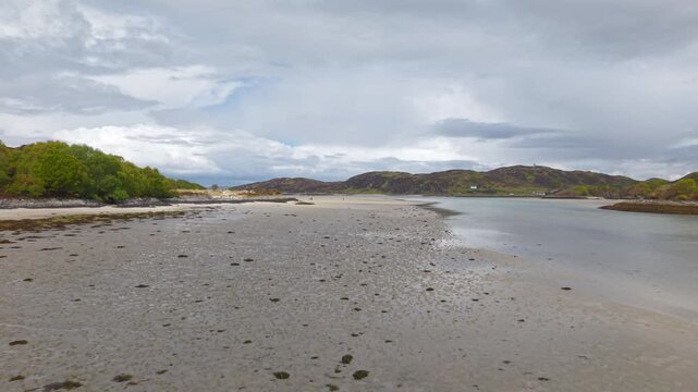 Wide drone flight over the expansive sands of Morar Beach and the adjacent river estuary under a bright, overcast sky in the Scottish Highlands.