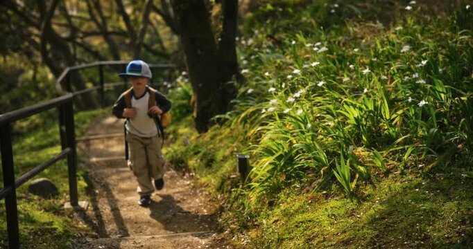 Adorable little boy with backpack and oversized hat walking up dirt trail in Japan - slow motion
