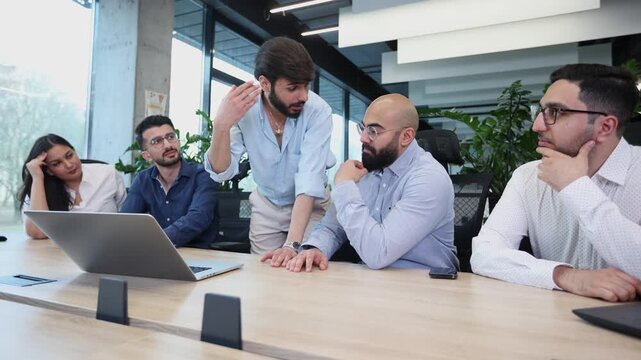 A group of people are sitting around a table with a laptop open