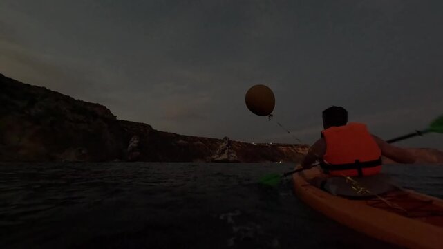 Kayak paddling ocean, person explores rocky coastline during evening twilight adventure