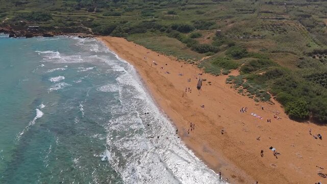 Ramla Beach in Gozo, Malta features its distinctive reddish sand and turquoise Mediterranean waters along the scenic coastline, viewed from an aerial perspective on a sunny day.