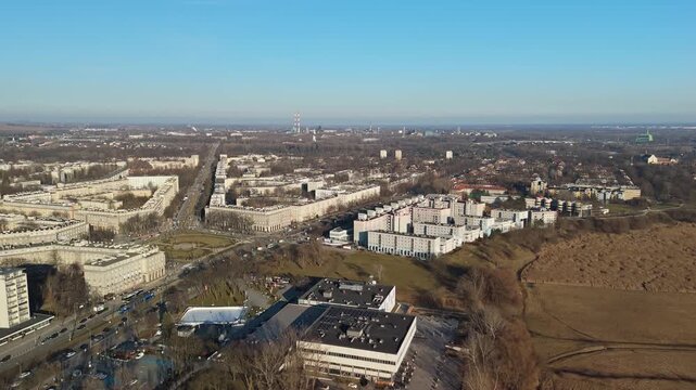 In Nowa Huta in Krak&oacute;w, an aerial view captures the residential blocks and structured urban layout surrounded by green spaces and industrial elements beneath a clear blue sky.