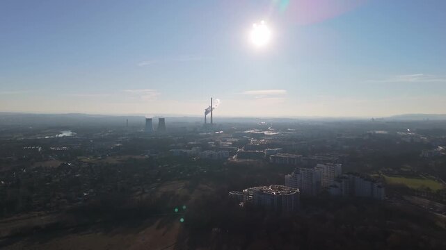 In Nowa Huta, Krak&oacute;w, residential apartment blocks and industrial facilities border the Łąki Nowohuckie park in an expansive urban landscape captured from an aerial perspective.