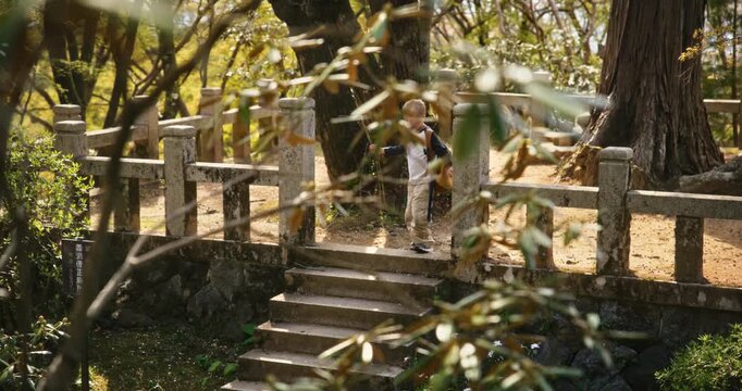Blond boy walking along ancient stone platform in Japanese forest - steady cam shot