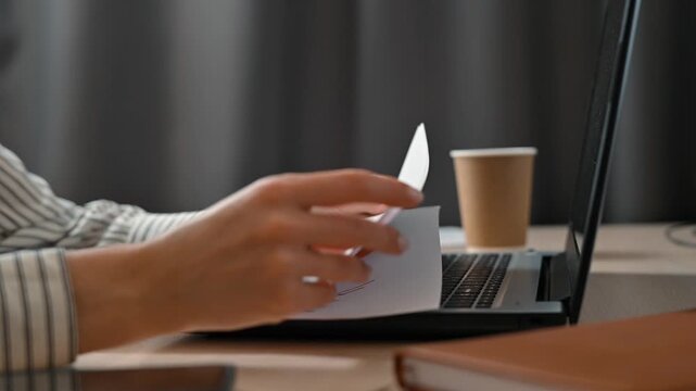 A person engages in work by reviewing documents and typing notes on a laptop in an office environment