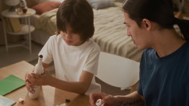 Asian father and multiethnic child building toy space rocket together at wooden table. Footage ideal for commercials promoting STEM education, creative toys, and family bonding