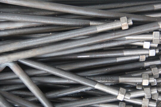 Close-up of steel threaded rods with nuts and bolts stacked in an industrial workshop. Metal fasteners background, construction hardware, engineering and manufacturing concept.