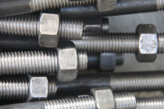 Close-up of steel threaded rods with nuts and bolts stacked in an industrial workshop. Metal fasteners background, construction hardware, engineering and manufacturing concept.