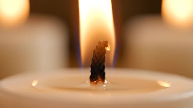 Close up of burning candle wick with orange flame and soft bokeh background
