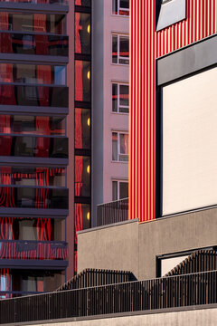 Red facade detail in Oslo, Norway, shows a modern apartment building where residential architecture sets balcony rails beside deep urban shadow