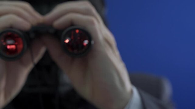 Man in a suit and gorilla mask using binoculars, zooming in on the viewer against a blue background