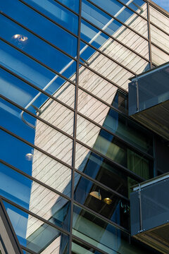 Blue glass facade beside a modern office building shows abstract architecture, balcony edge, reflection, and diagonal urban lines under sky