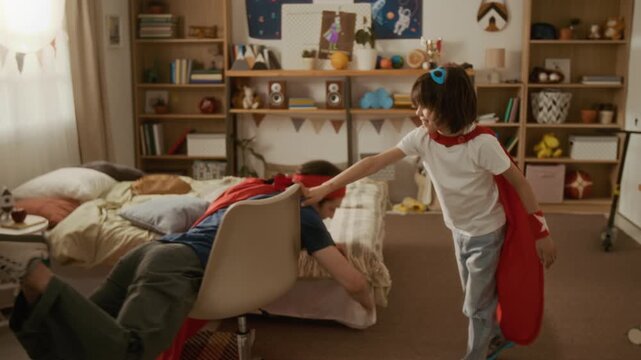 Young father and son wearing superhero capes playing in bedroom, father pretending to fly on rolling chair. Perfect for family lifestyle ads and parenting campaigns