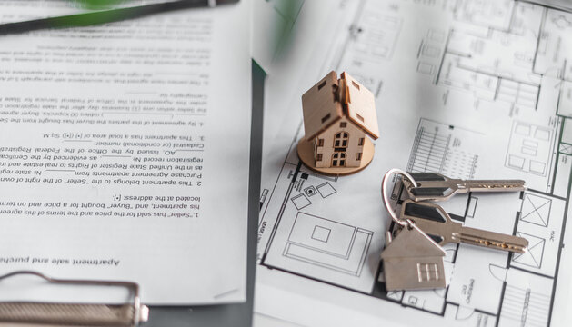 Architectural drawings, purchase and sale agreement and symbolic house model highlight careful preparation for purchasing property. Home financing, legal paperwork, creating stable living conditions