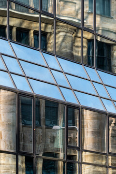 Blue reflections cross a Frankfurt, Germany glass facade where modern financial architecture layers urban windows over a historic stone surface