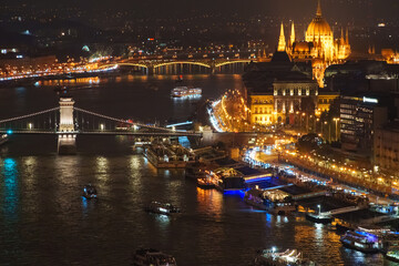 Obraz premium Night view of Budapest Hungary with illuminated Chain Bridge and Hungarian Parliament Building over Danube River featuring city lights and boats on water at night