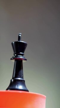 4K Video macro close up of a black chess king piece rotating smoothly on a red platform, symbolizing strategy, leadership, power, victory, and intellectual competition against a moody gray out