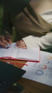 A professional is meticulously writing notes in a red notebook, focusing on business details. This scene captures diligent hands planning and documenting important work tasks