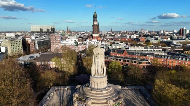 Aerial view of the Bismarck Monument surrounded by green trees with the St. Michael's Church tower in the background under a blue sky Hamburg, Hamburg, Germany.