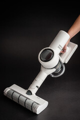 Close up of a woman holding a white cordless vacuum cleaner with motorized floor brush, handheld cleaning process on a black background. © Serhii