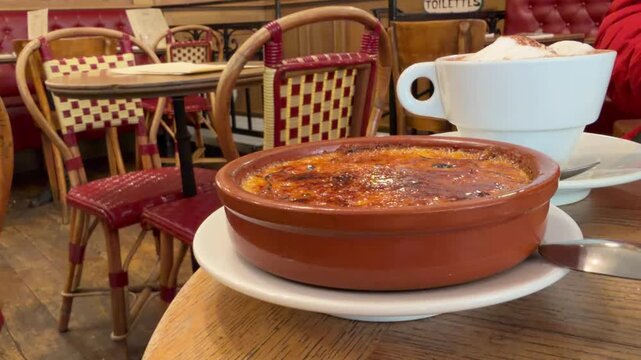Steaming cr&egrave;me br&ucirc;l&eacute;e and a hot cappuccino resting on a wooden table in a classic Parisian bistro. This close-up highlights the quintessential French dessert experience during a European vacation