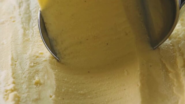 4K Video of a professional metal scoop rolling a perfect ball of creamy vanilla bean ice cream with specks, creating a smooth texture in a tub, ideal for sweet summer dessert commercials and food mark