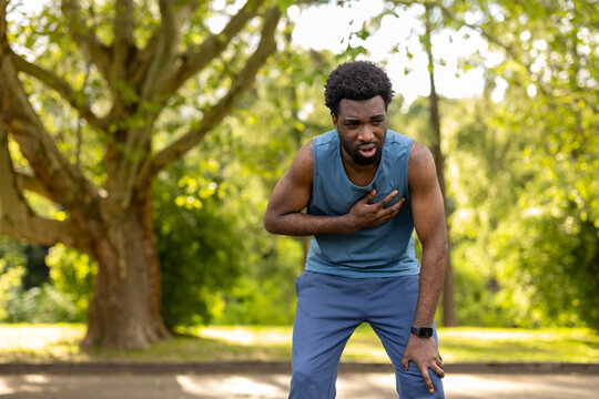 Young adult man stopping his outdoor run due to sudden chest discomfort, indicating a potential health emergency or cardiovascular issue while exercising alone in a park