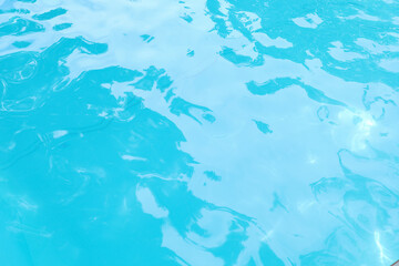 Top view of crystal clear blue swimming pool water texture with gentle ripples and sunlight reflections for summer background.