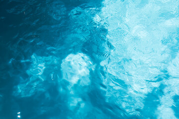 Obraz na płótnie Canvas Top view of crystal clear blue swimming pool water texture with gentle ripples and sunlight reflections for summer background.