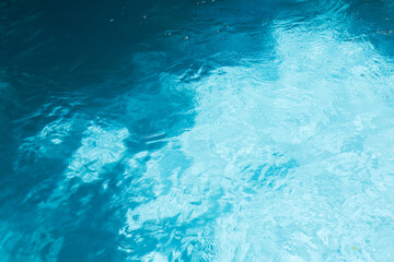 Obraz na płótnie Canvas Top view of crystal clear blue swimming pool water texture with gentle ripples and sunlight reflections for summer background.