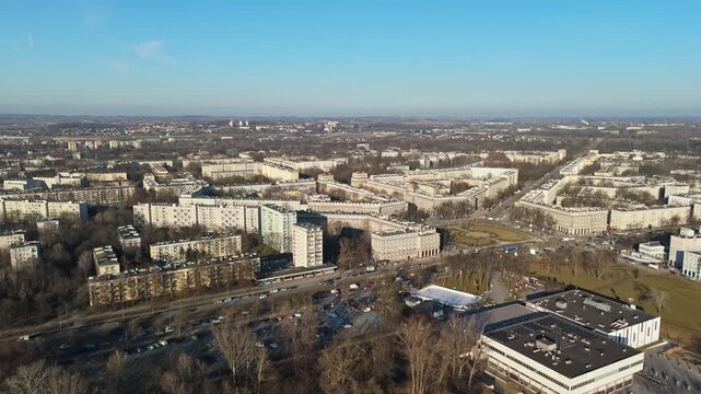 In Nowa Huta, Krak&oacute;w, residential apartment blocks and public spaces form a planned urban layout surrounding a main avenue and intersection, viewed by drone under a clear blue sky.