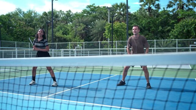 Mixed doubles pickleball teammates celebrating a successful play by tapping paddles, representing teamwork, achievement, sportsmanship, and positive recreation