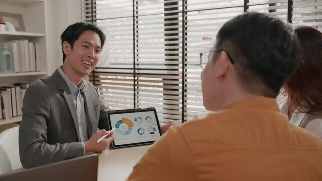Male financial advisor presenting savings or investment strategies to a young Asian couple. Advisor smiling and shaking hands with client to close a deal. Wealth management, real estate investment.