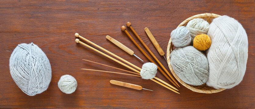 Arrangement of skeins of natural wool yarn in wicker basket and knitting needles and crochet hooks on wooden table. Concept of handicrafts and creativity. Flat lay, copy space, top view, closeup