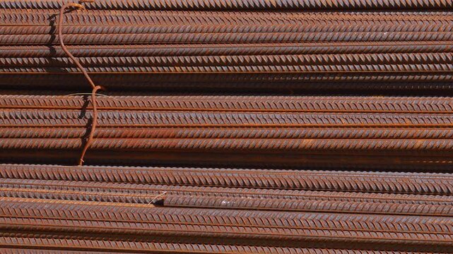 Rusty steel reinforcing bars stacked horizontally in bundles at a construction site, creating a textured industrial background of corroded metal rods used for strengthening concrete structures