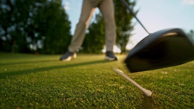 4K Video of a golfer taking a powerful swing, hitting a white golf ball off the tee on a lush green course during a beautiful, bright sunset with lens flare, capturing active sports and outdoor