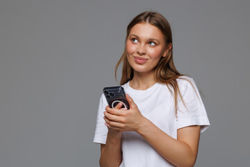 Fototapeta premium Smiling woman using phone, looking at her phone with happy face, reading, standing over white background