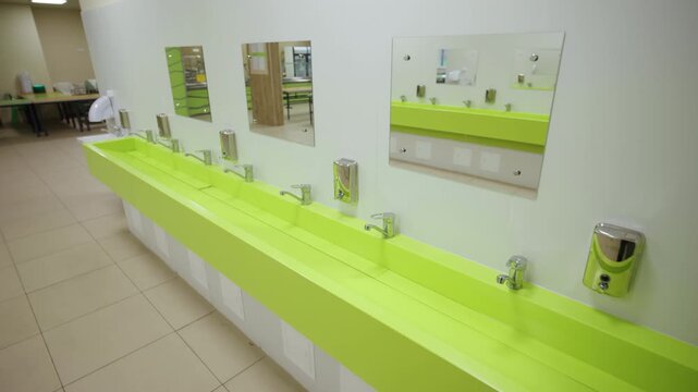 Green hand wash basin with chrome taps and mirrors in school canteen. Public open washbasin for children in empty cafeteria lobby