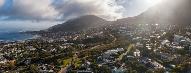 Aerial panorama of Cape Town, South Africa, shows Twelve Apostles and Table Mountain, Atlantic on the left, whitewashed houses, winding roads, low clouds, and rim light. © Aerial Film Studio