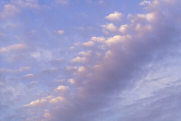 Fototapeta premium A beautiful sky with clouds that are white, purple and pink tinted at sunset against a blue sky. 