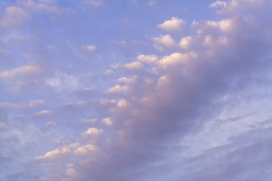 A beautiful sky with clouds that are white, purple and pink tinted  at sunset against a blue sky.
