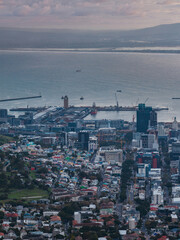 Obraz premium Aerial view of Cape Town city center and Victoria and Alfred Waterfront shows piers, cranes, vessels, mid and high rises, homes, parkland, dusk light, mountains, clouds.